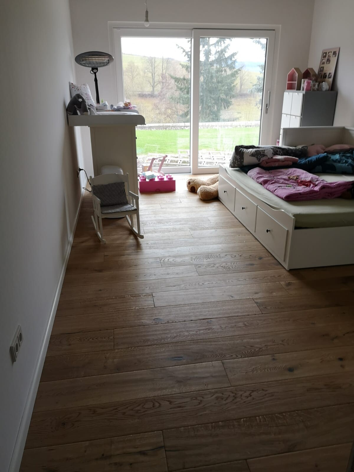 Kinderzimmer: weißes Bett mit Stauraum, Spielzeug, großes Fenster mit Gartenblick.