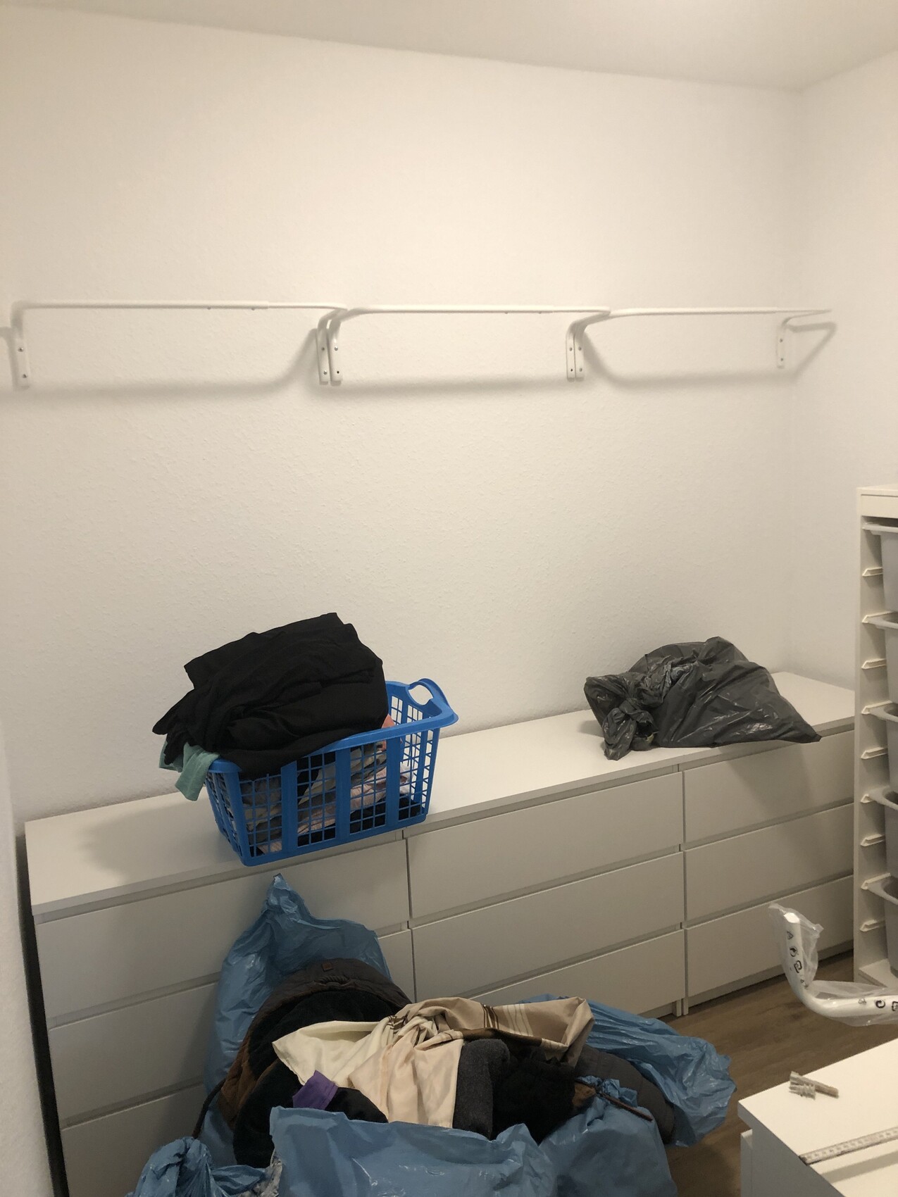 Kleiderschrank-Abstellraum mit weißen Schubladen, Wäschekorb, Kleidung und Müllsäcke