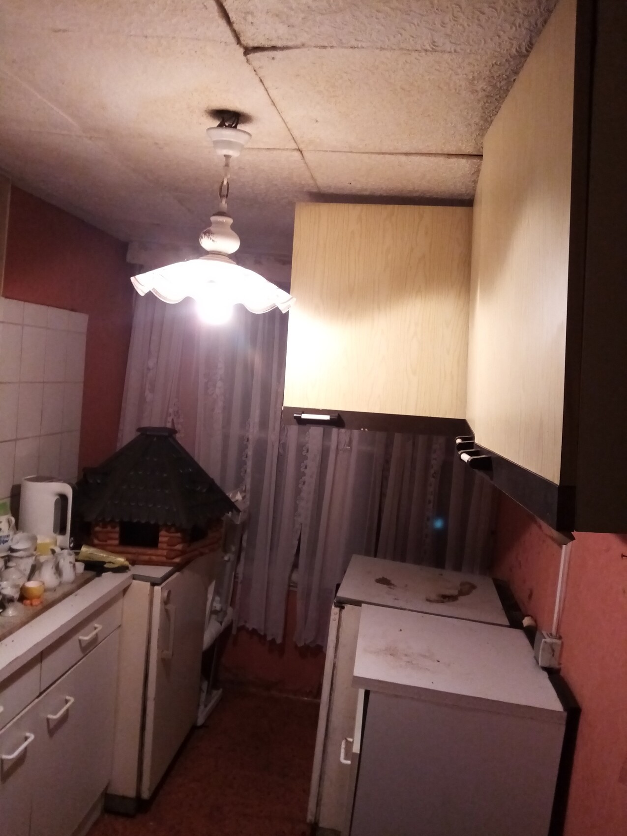 Küche mit einer hängenden Lampe, weißen Schränken und Holzhaus-Deko auf der Arbeitsfläche.