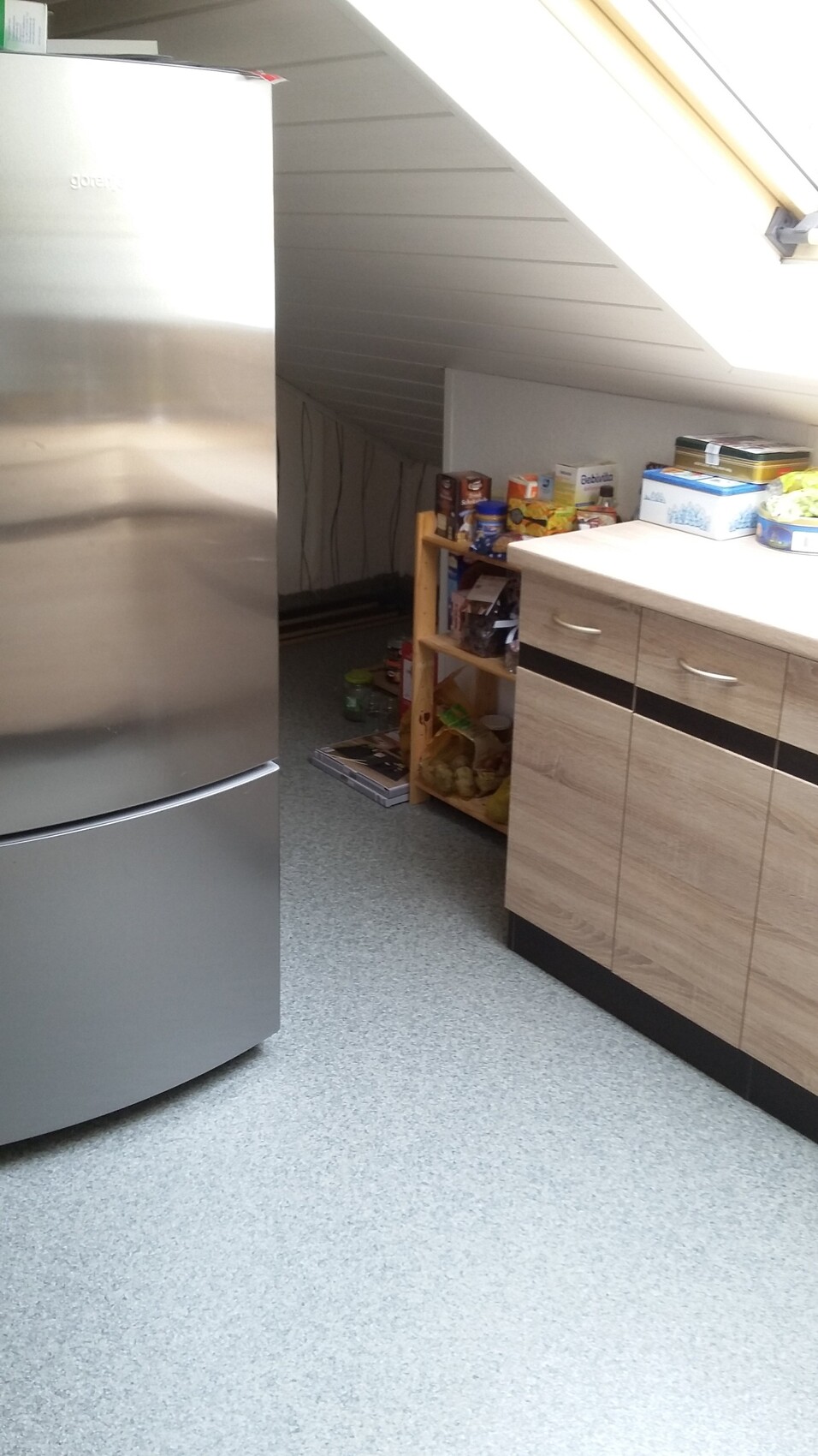 Küche mit Edelstahlkühlschrank, unter Dachschräge, Holzschränken und offenem Vorratsregal.