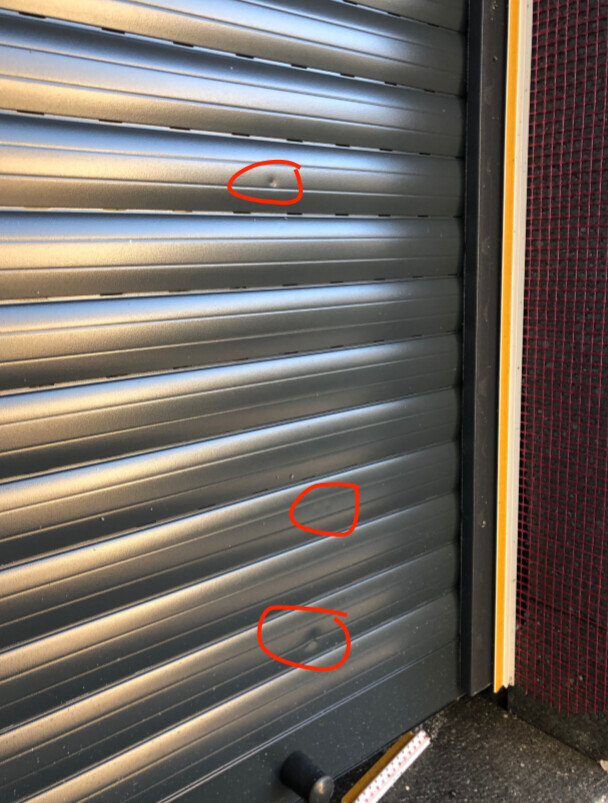 Dunkelgrauer Rollladen mit drei kleinen Dellen, rot markiert.