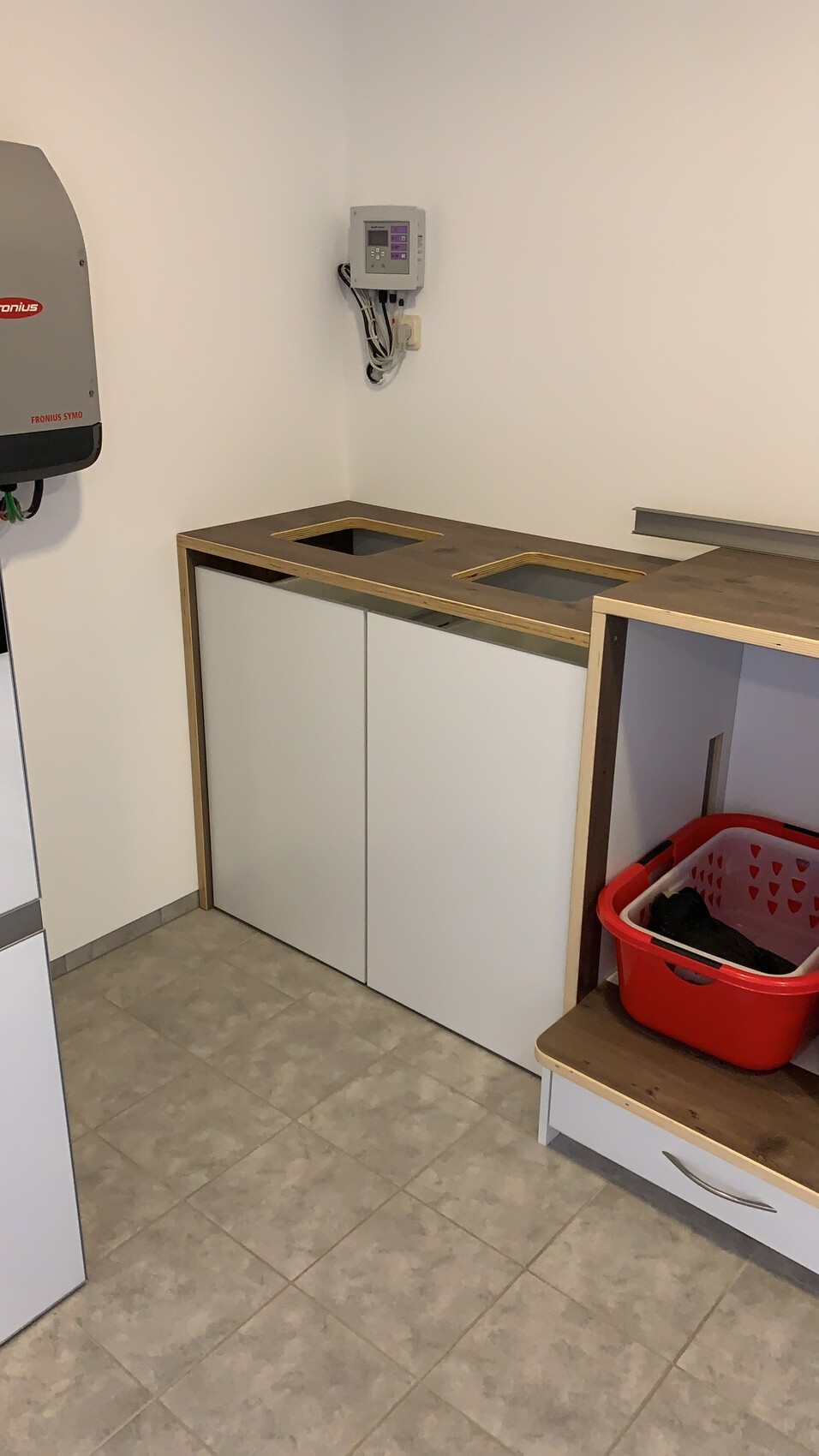Küchenunterschrank mit Holzplatte und zwei Spülenaussparungen, roter Wäschekorb daneben.