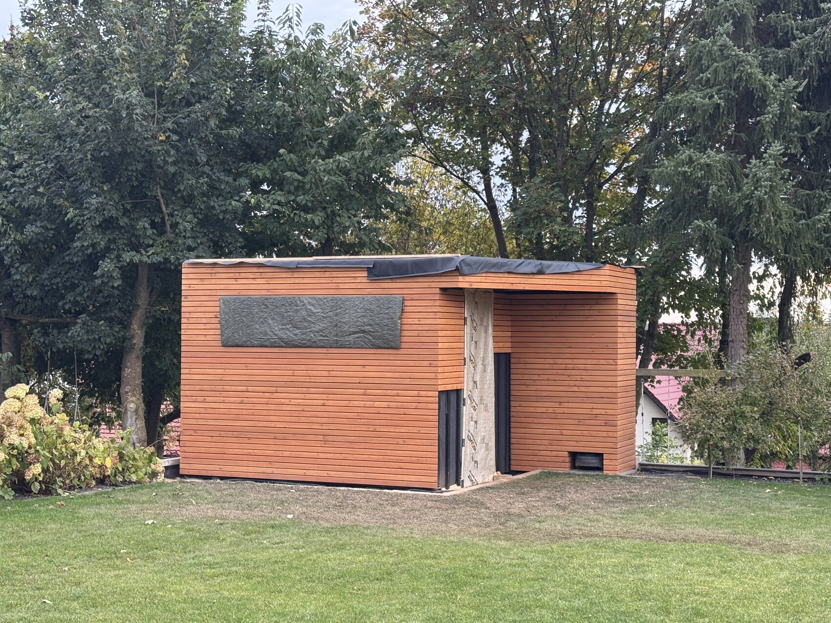 Kleiner orangefarbener Holzschuppen im Garten, von Bäumen umgeben.
