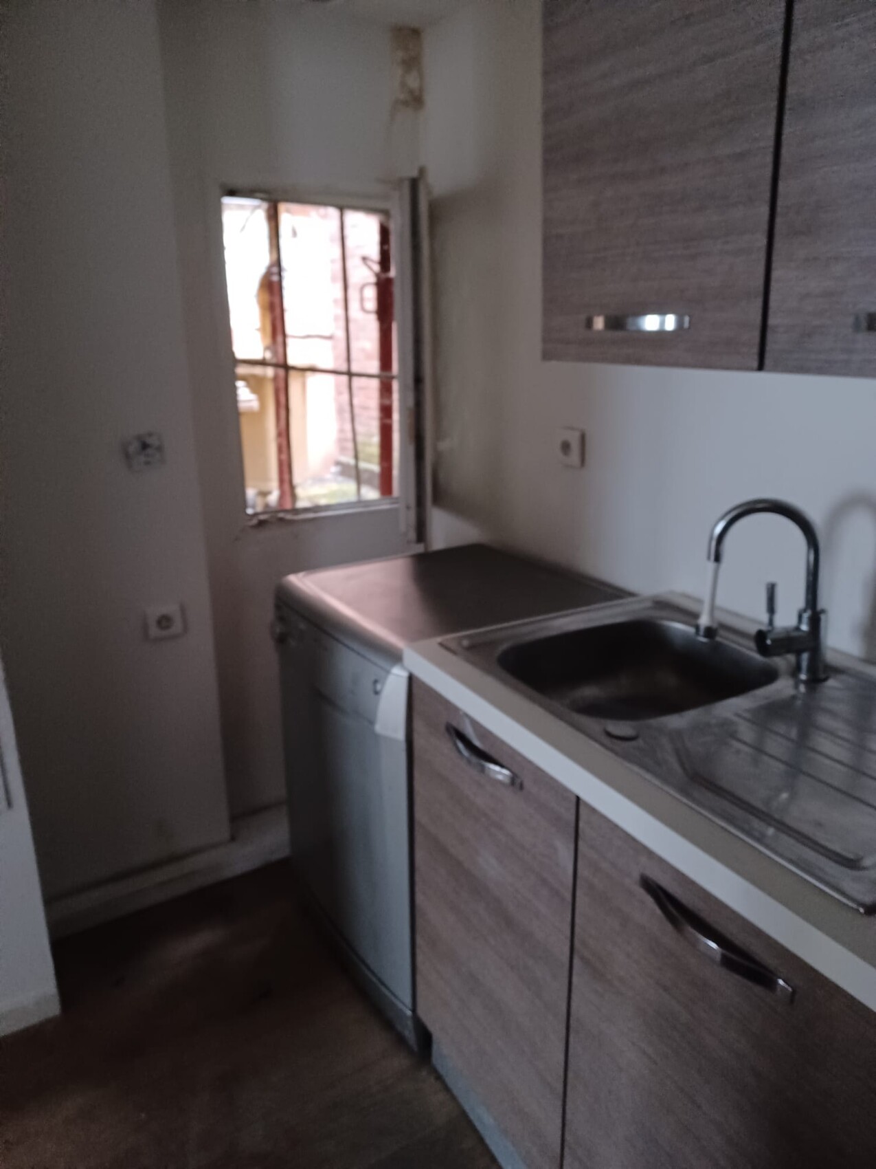 Kleine Küche mit Spüle, Spülmaschine, Holz-Fronten, Fenster mit Gitter.