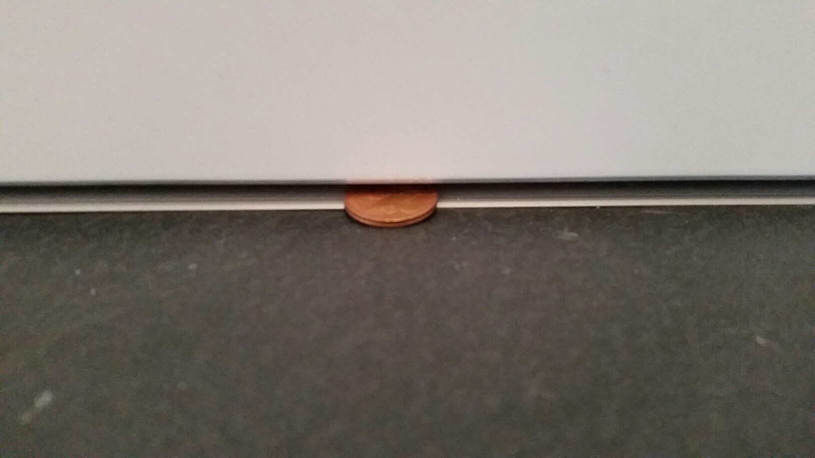 Eine kleine kupferfarbene Münze steckt im Spalt unter einer Tür am dunklen Boden.