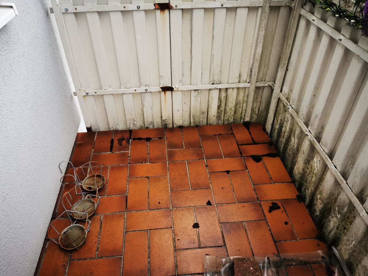 Kleiner Hof mit orange Terracottafliesen, rostigen weißen Zäunen und Pflanzkörben.
