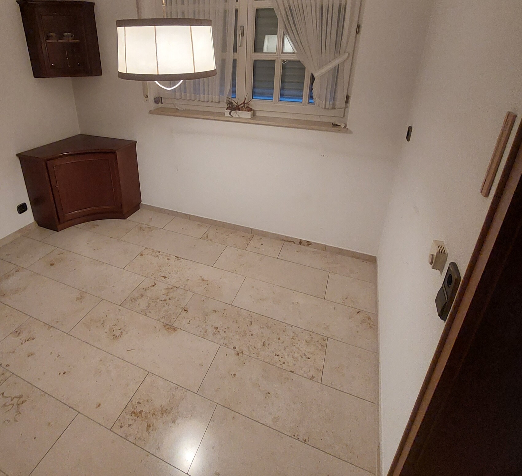 Leeres Zimmer mit beige Fliesenboden, hängendem Lampenschirm, Fenster mit Vorhängen und Holzmöbel.
