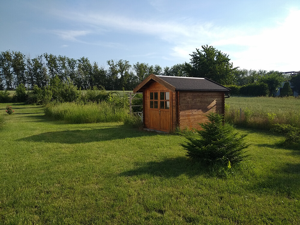Holzhütte im grünen Garten, Baumreihe im Hintergrund, sonniger Tag