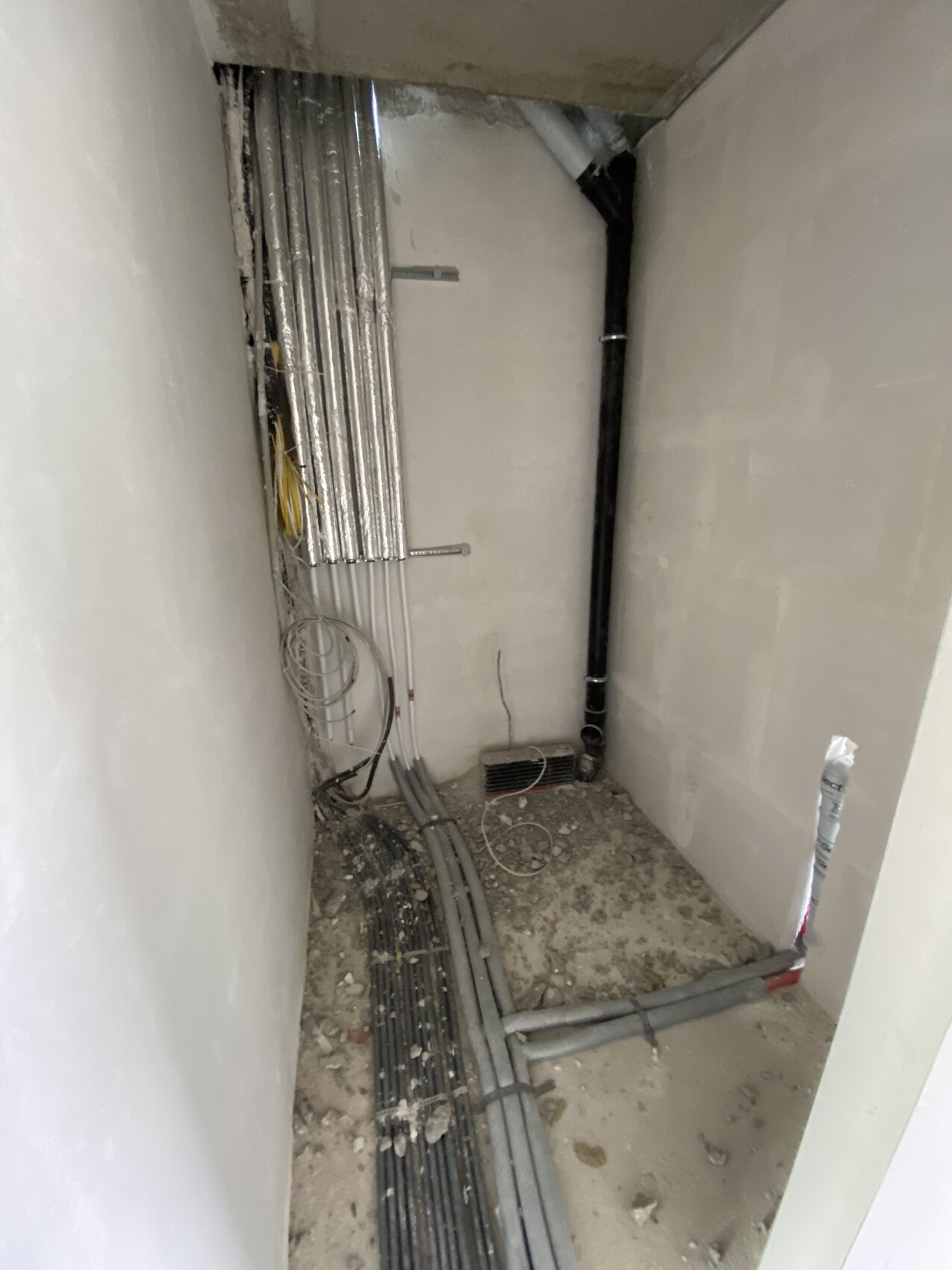 Kabelkanäle, Rohre und lose Kabel in einem engen unfertigen Technikraum.