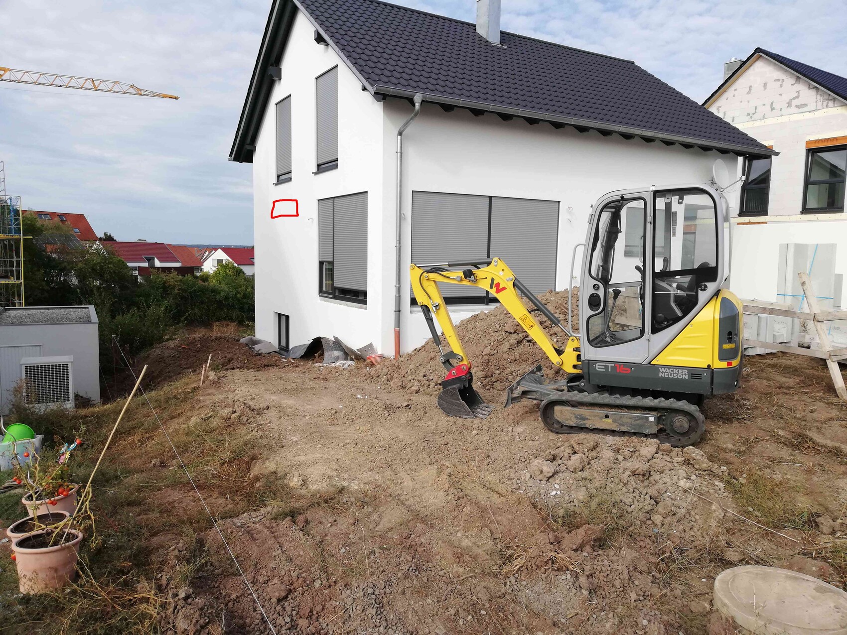 Gelber Minibagger auf Baustelle neben einem weißen Haus mit Rollläden.
