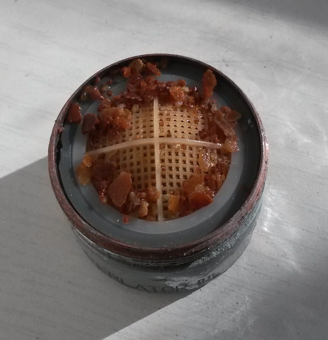 Kleiner runder Grinder mit Sieb und braunen Resten auf Metalltisch