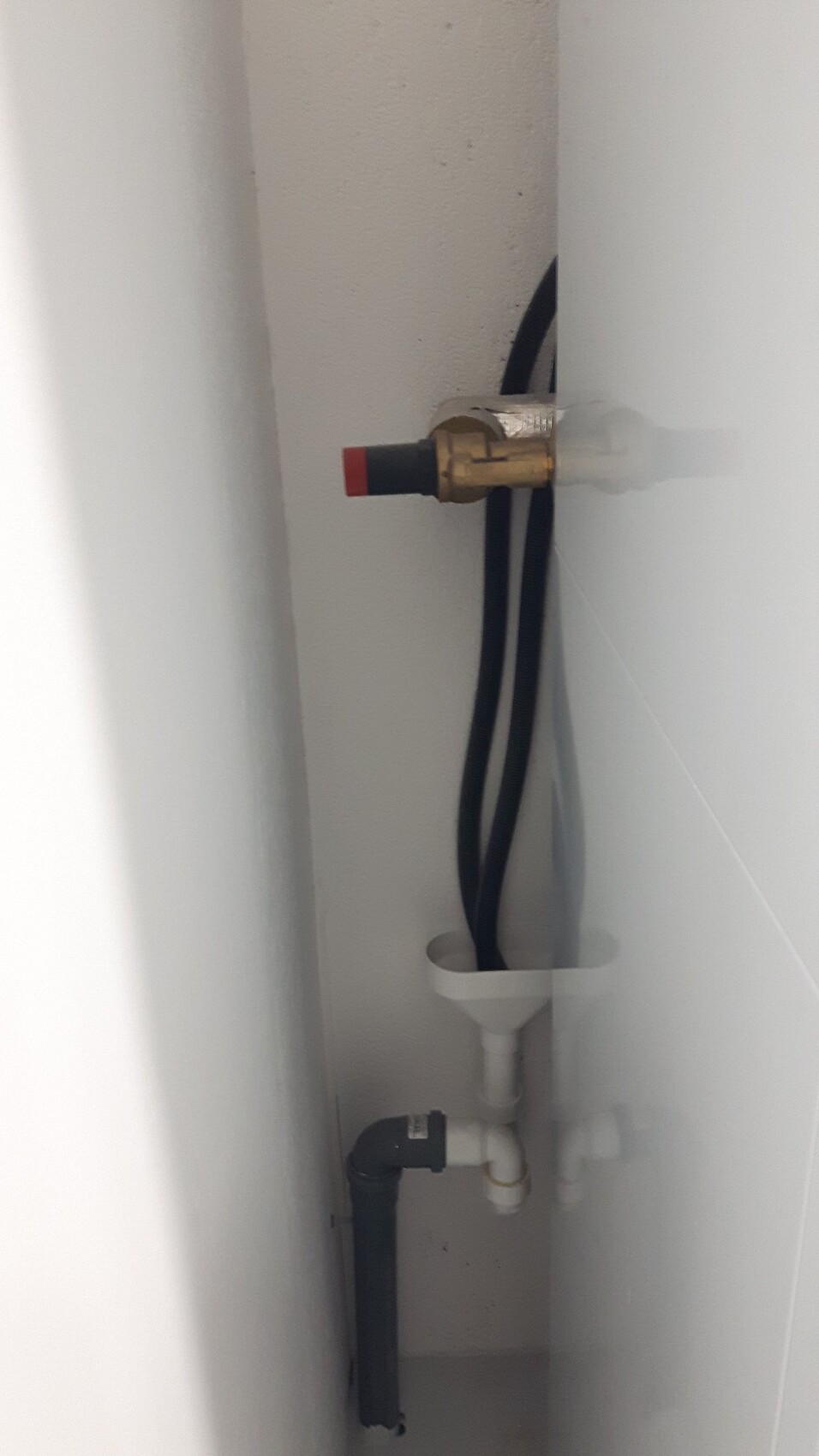 Unter Spülenschrank sichtbare Wasserleitungen, Ventil mit roter Kappe, Schläuche und Abflussrohr.