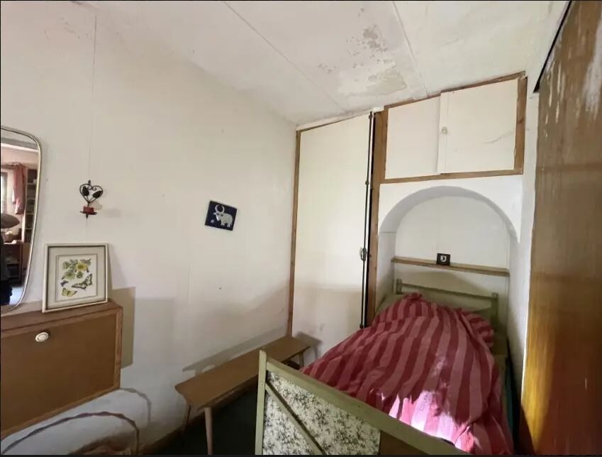 Kleines Schlafzimmer mit Einzelbett, roter gestreifter Decke, Spiegelkommode links und Wandnische.