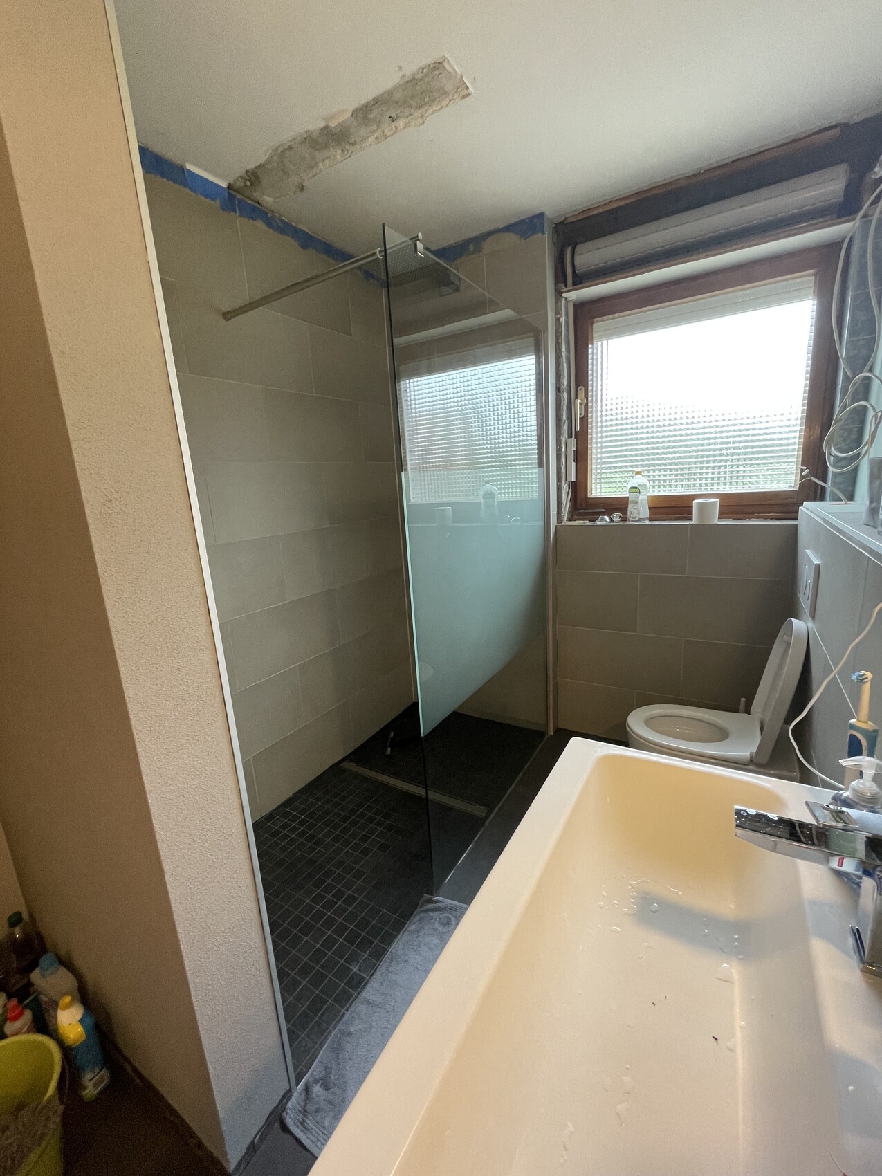 Badezimmer mit Glasdusche, Waschbecken, WC; Fenster mit Sichtschutz, Renovierungsarbeiten sichtbar.