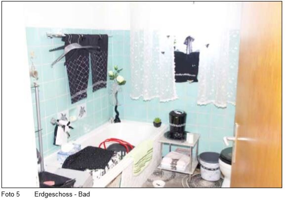 Badezimmer mit Badewanne, Wäsche zum Trocknen an einer Stange, türkisfarbene Fliesen und Vorhänge.