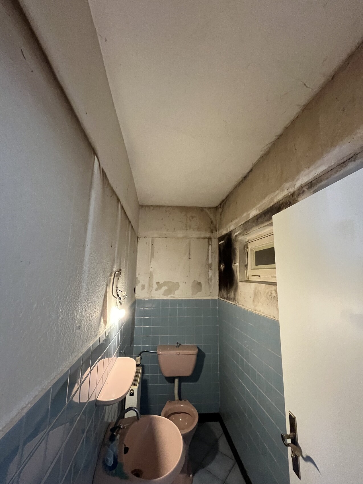 Kleines Bad mit blauen Fliesen, Toilette und Waschbecken, beschädigte Wände