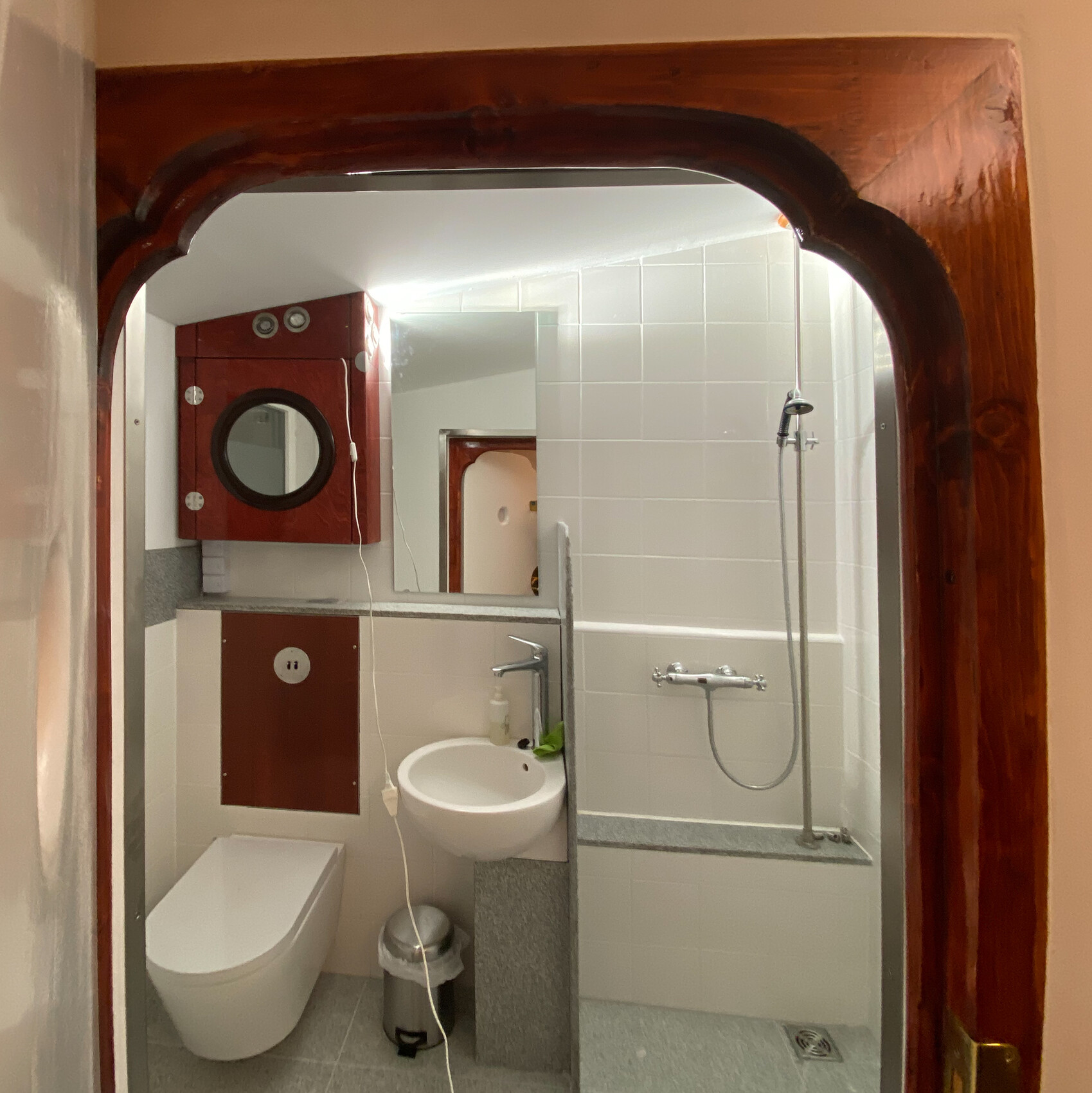 Kleines Badezimmer mit Toilette, Waschbecken, Dusche und Holzrahmen-Türbogen