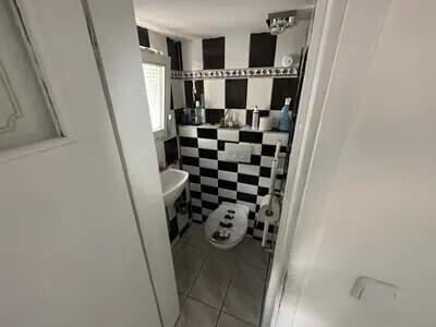 Kleines Badezimmer mit schwarz-weissen Fliesen, Toilette und Waschbecken, Fenster seitlich.