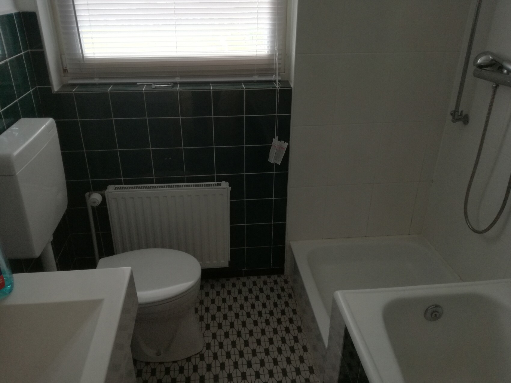 Kleines Badezimmer mit Toilette, Waschbecken, Badewanne, Dusche und dunklen Fliesen.