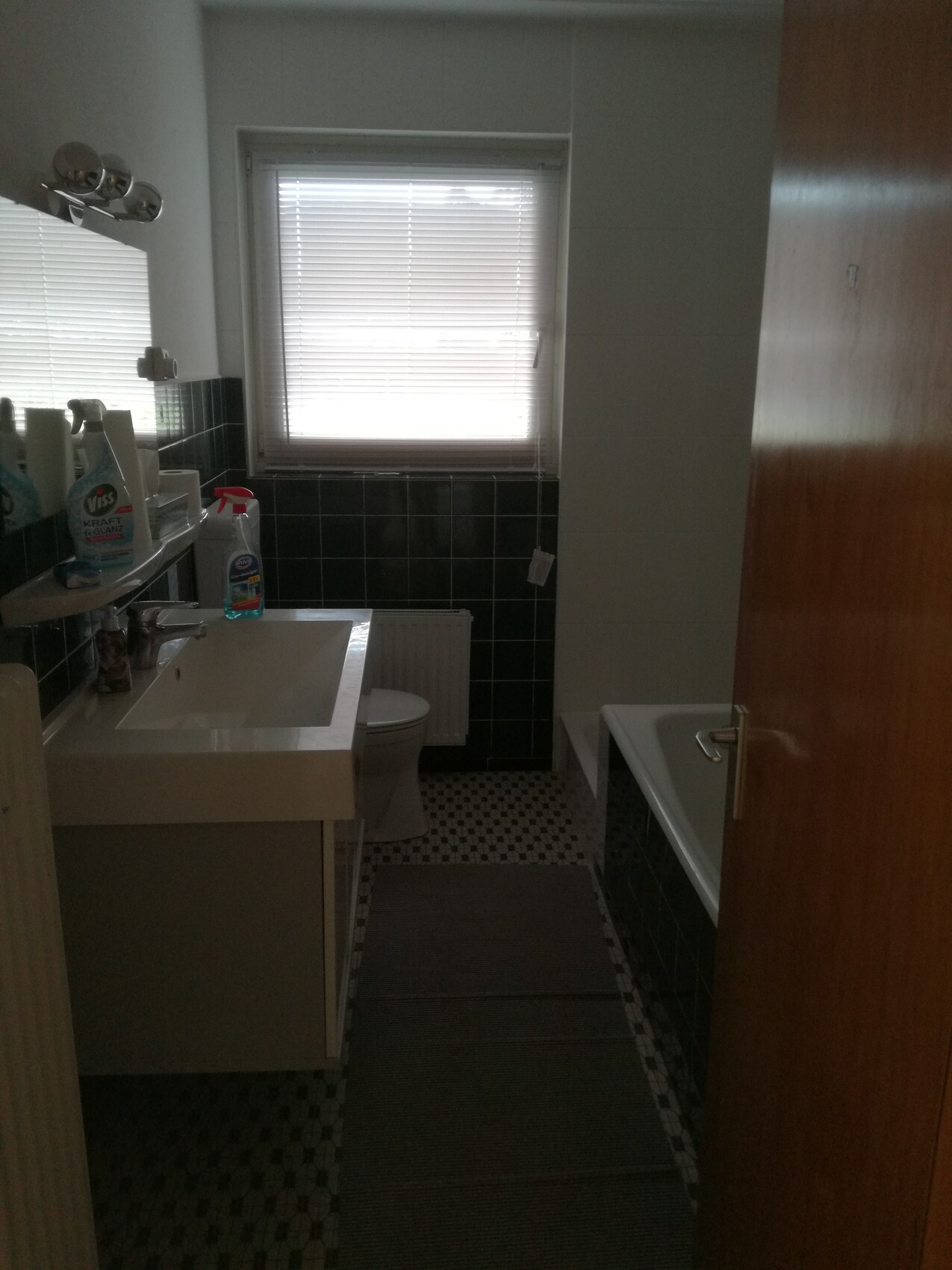 Kleines Badezimmer mit Waschbecken, Spiegel, Fenster mit Jalousien, Toilette und Badewanne.