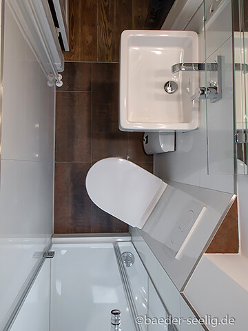 Kleines Badezimmer mit Waschbecken, Toilette und Dusche hinter Glas