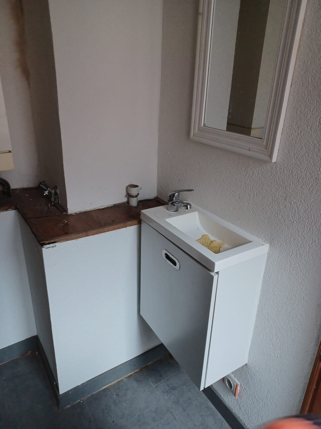 Kleines Waschbecken mit weißem Unterschrank, Armatur, Spiegel, Spülschwamm im Becken