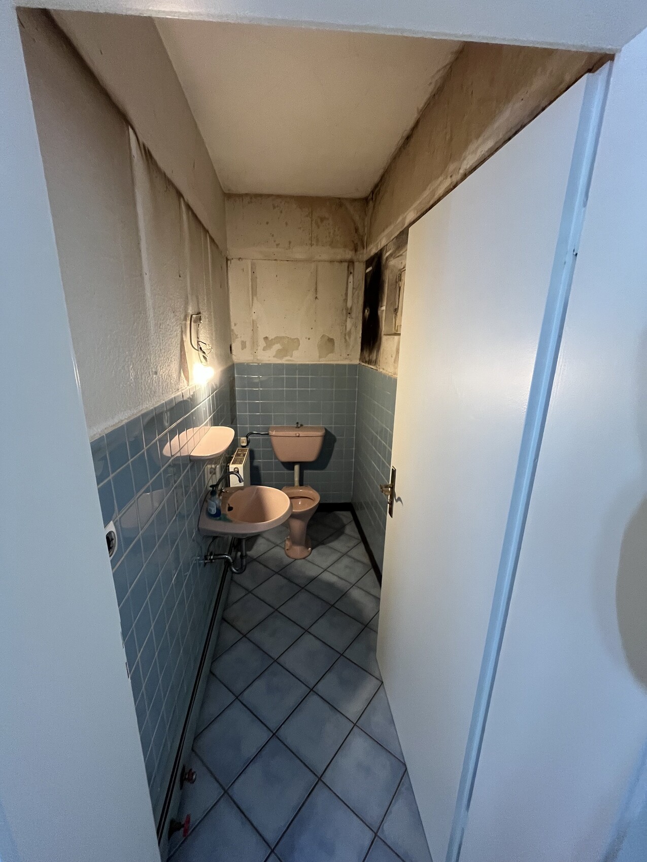 Kleines Bad mit blauen Fliesen, Toilette und Waschbecken in engem Raum.