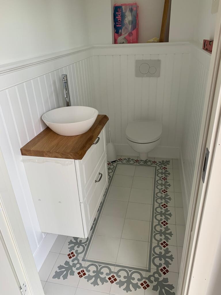 Kleines Bad: weiße Paneelwand, Vessel-Becken auf Holzplatte, wandhängende Toilette, Fliesenbordüre.