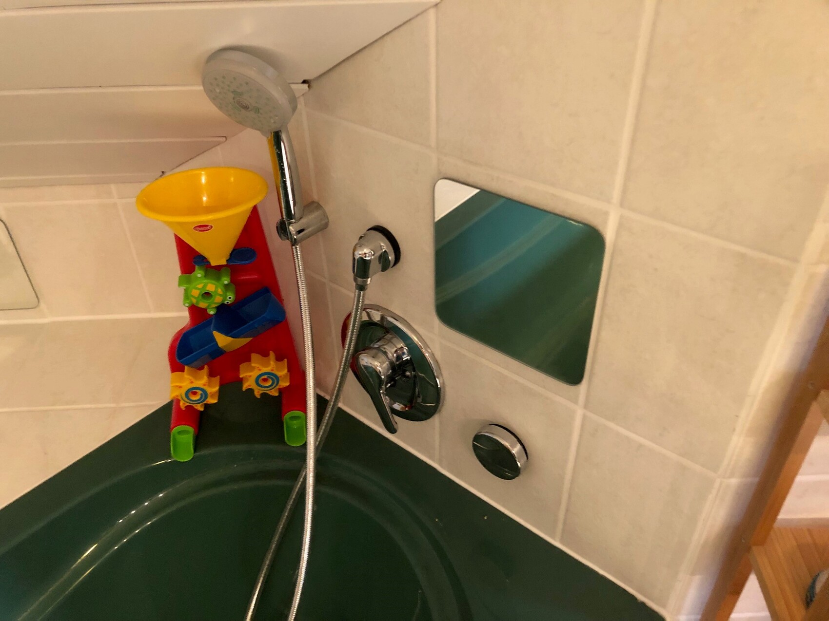 Buntes Badespielzeug in der Badewanne: gelber Trichter auf rotem Stativ, Duschkopf und Armatur.