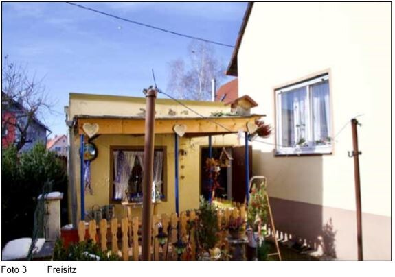 Kleines gelbes Haus mit blauer Veranda, Herz-Dekoration und Zaun im Vorgarten