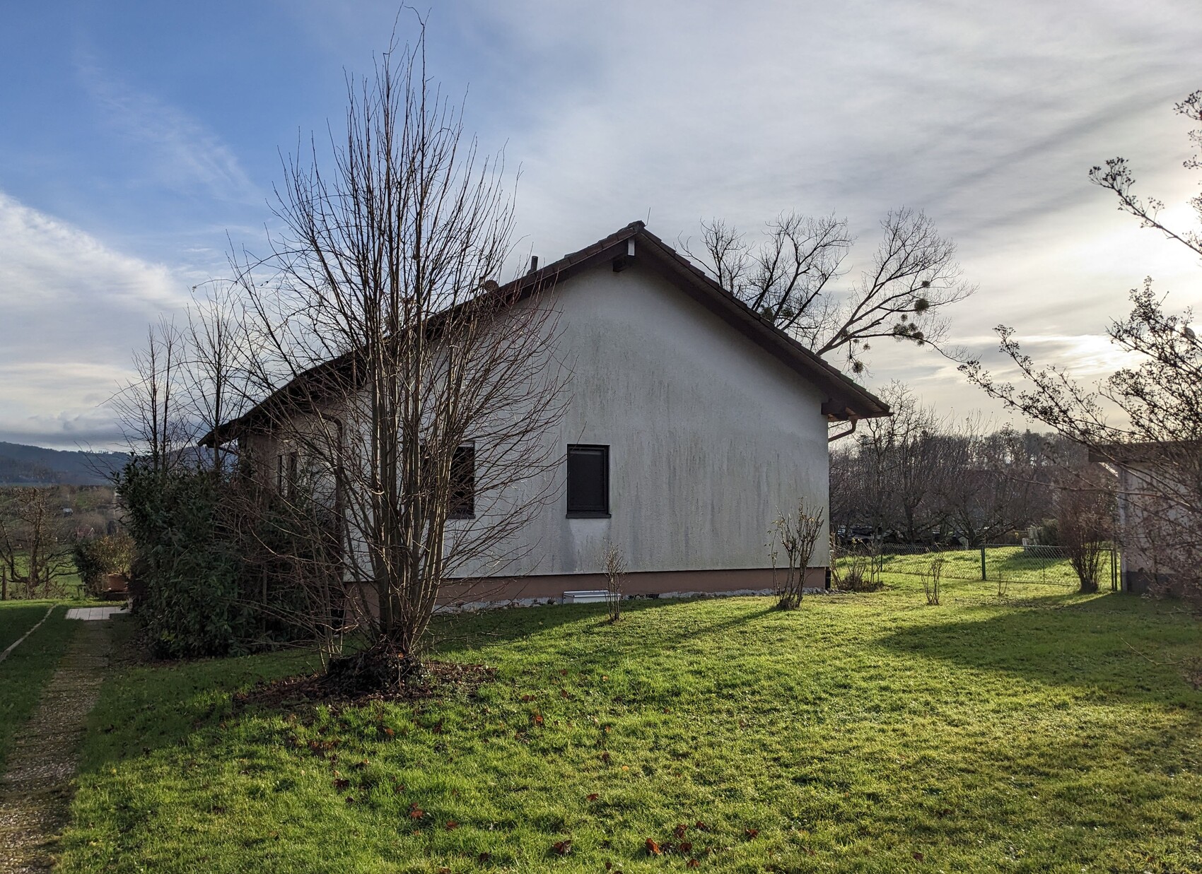 Außenansicht eines kleinen Einfamilienhauses mit grünem Garten und Bäumen.