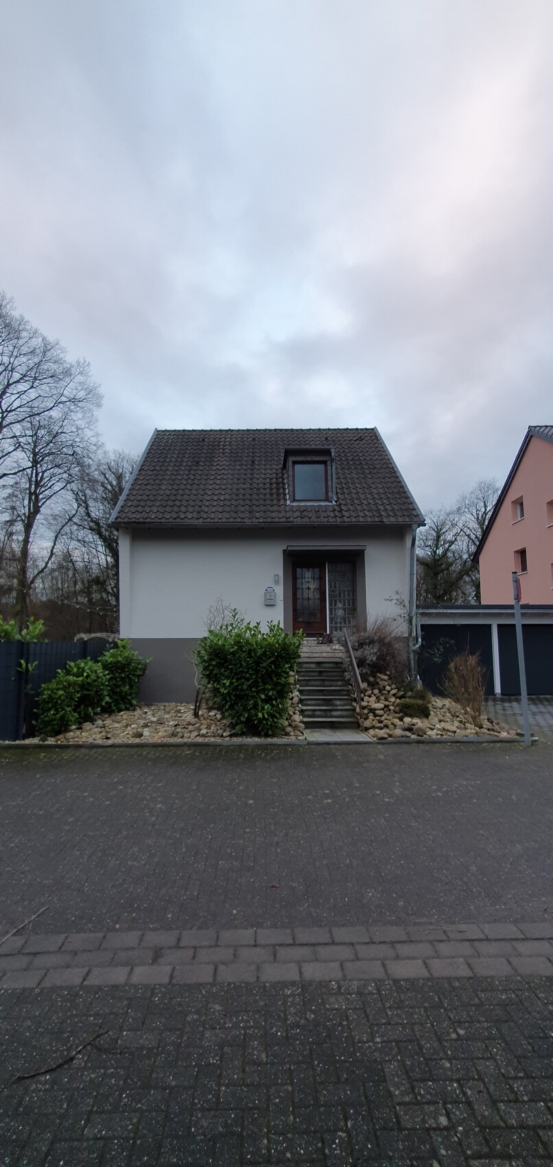 Kleines weißes Haus mit braunem Dach, Treppe zum Eingang und Steingarten.