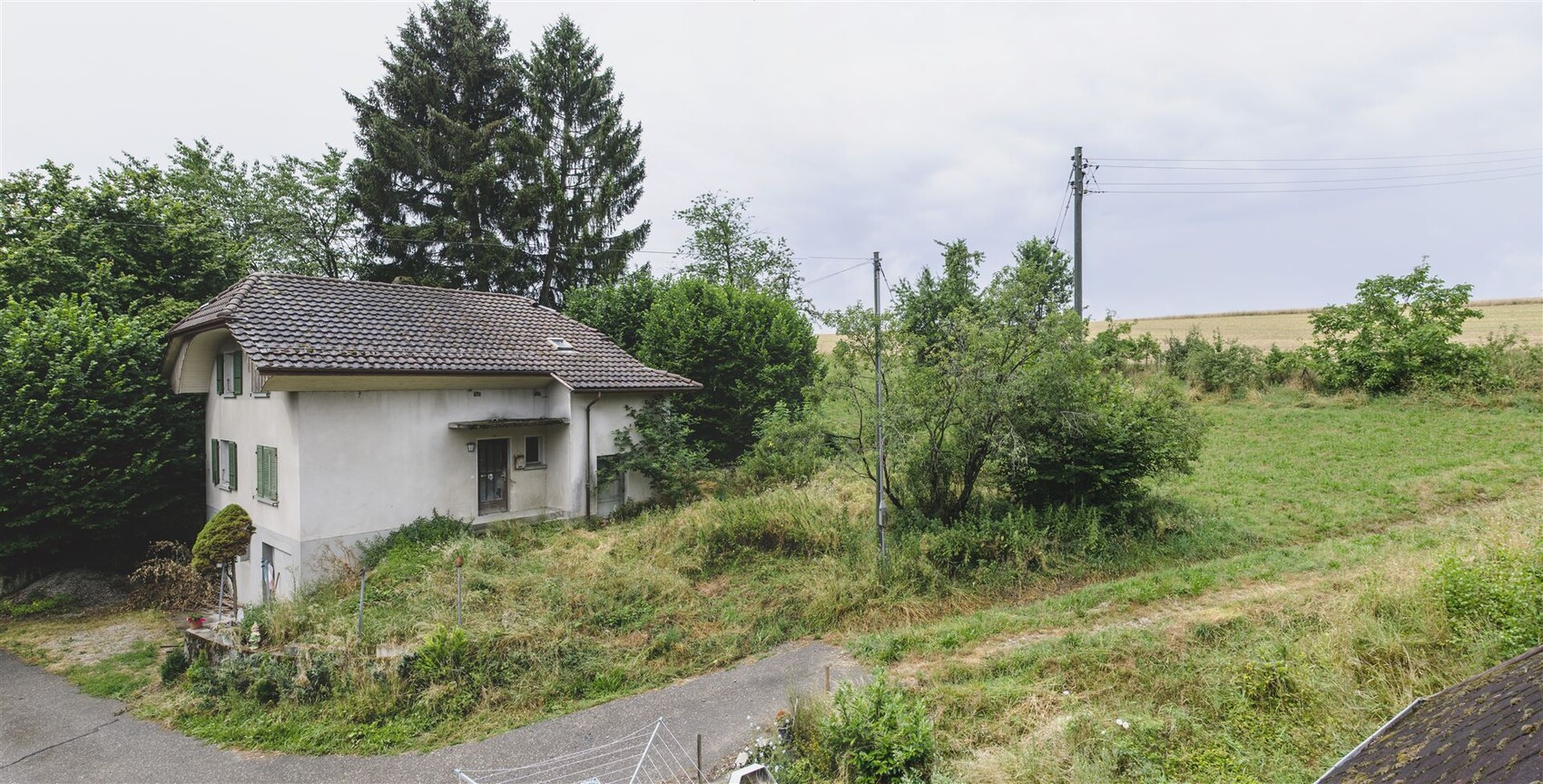 Kleines weisses haus mit rotem ziegeldach, gruenem garten, baeumen und stromleitung.