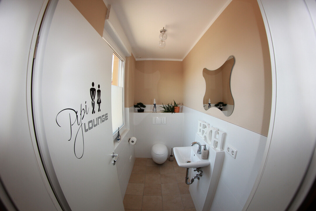 Kleines Badezimmer mit Waschbecken, Toilette, Pflanzen und unregelmäßigem Spiegel.