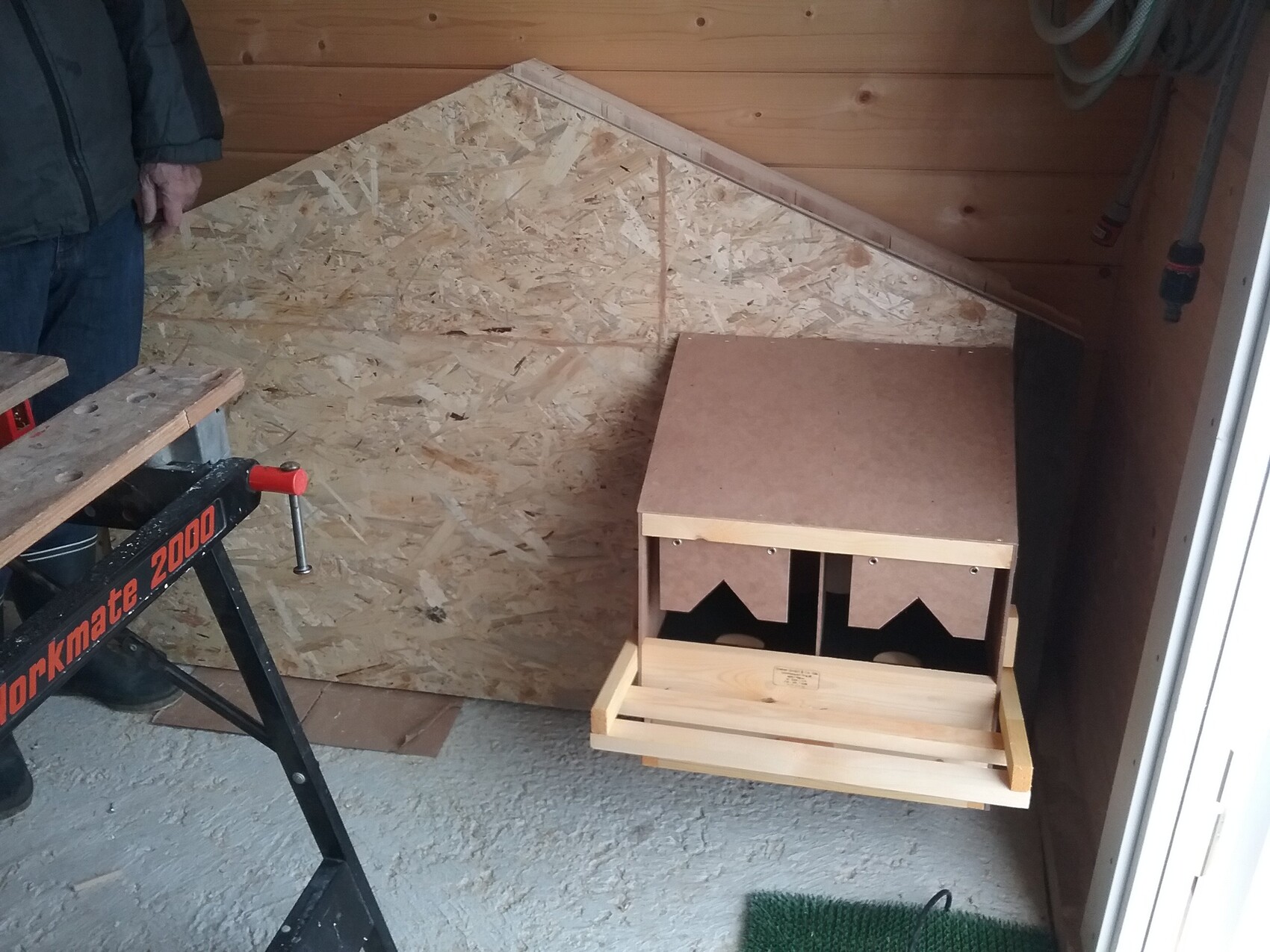 Eine Person steht neben einer Werkbank; im Vordergrund eine selbstgebaute Holzkiste mit zwei Fächern.