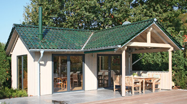 Kleines Holzhaus mit Terrasse vor Wald, gruenem Ziegeldach