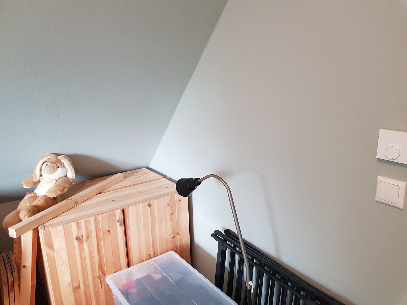 Kuschelhase sitzt auf einem Holzschrank unter schrägem Dach, neben einer biegsamen Lampe.