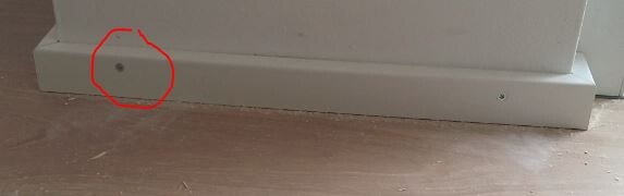 Kleines Loch in der weißen Sockelleiste direkt am Boden eines Innenraums