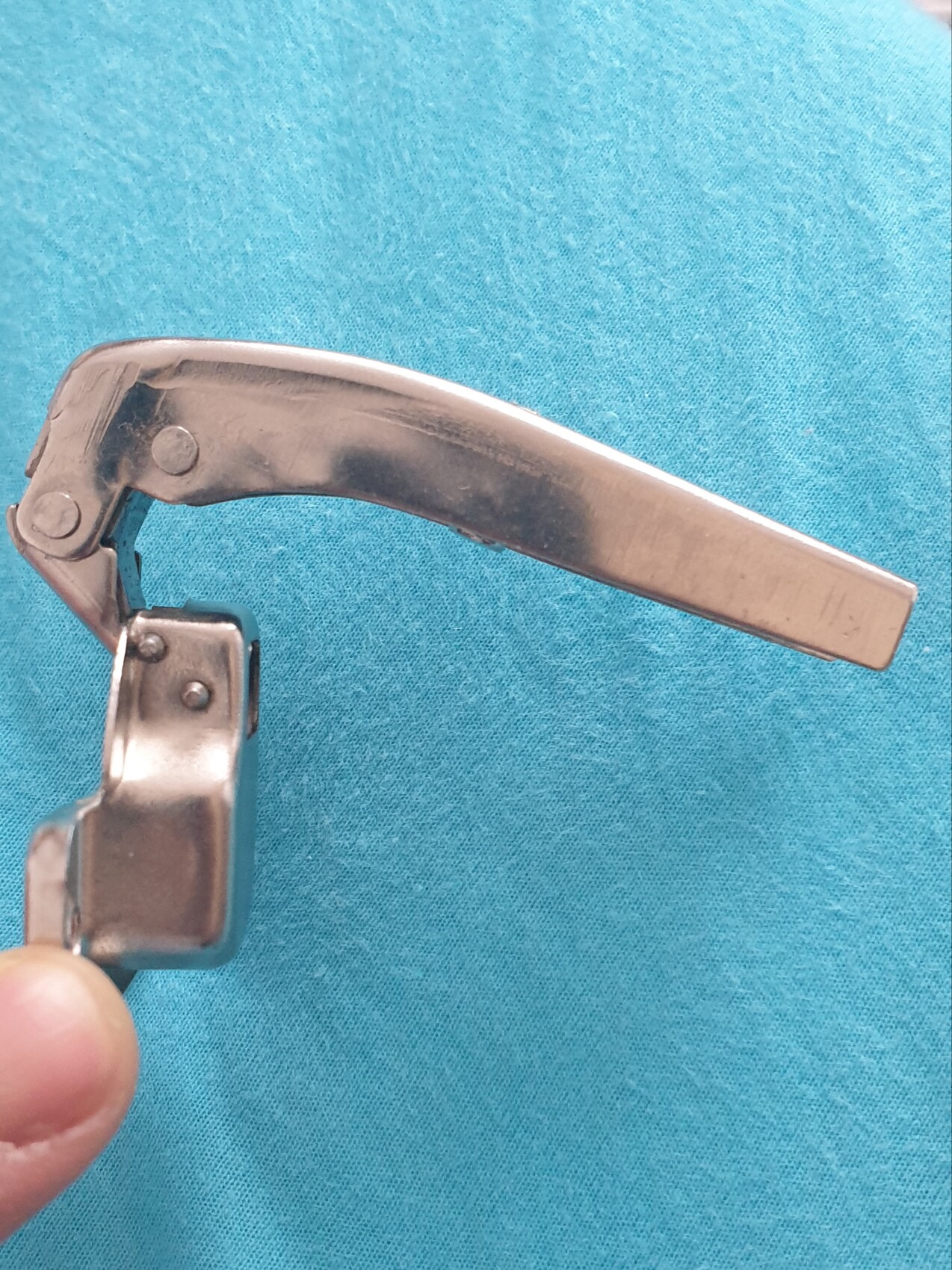 Metallischer Hebel mit Gelenk, Teil eines mechanischen Instruments, auf blauem Stoff.