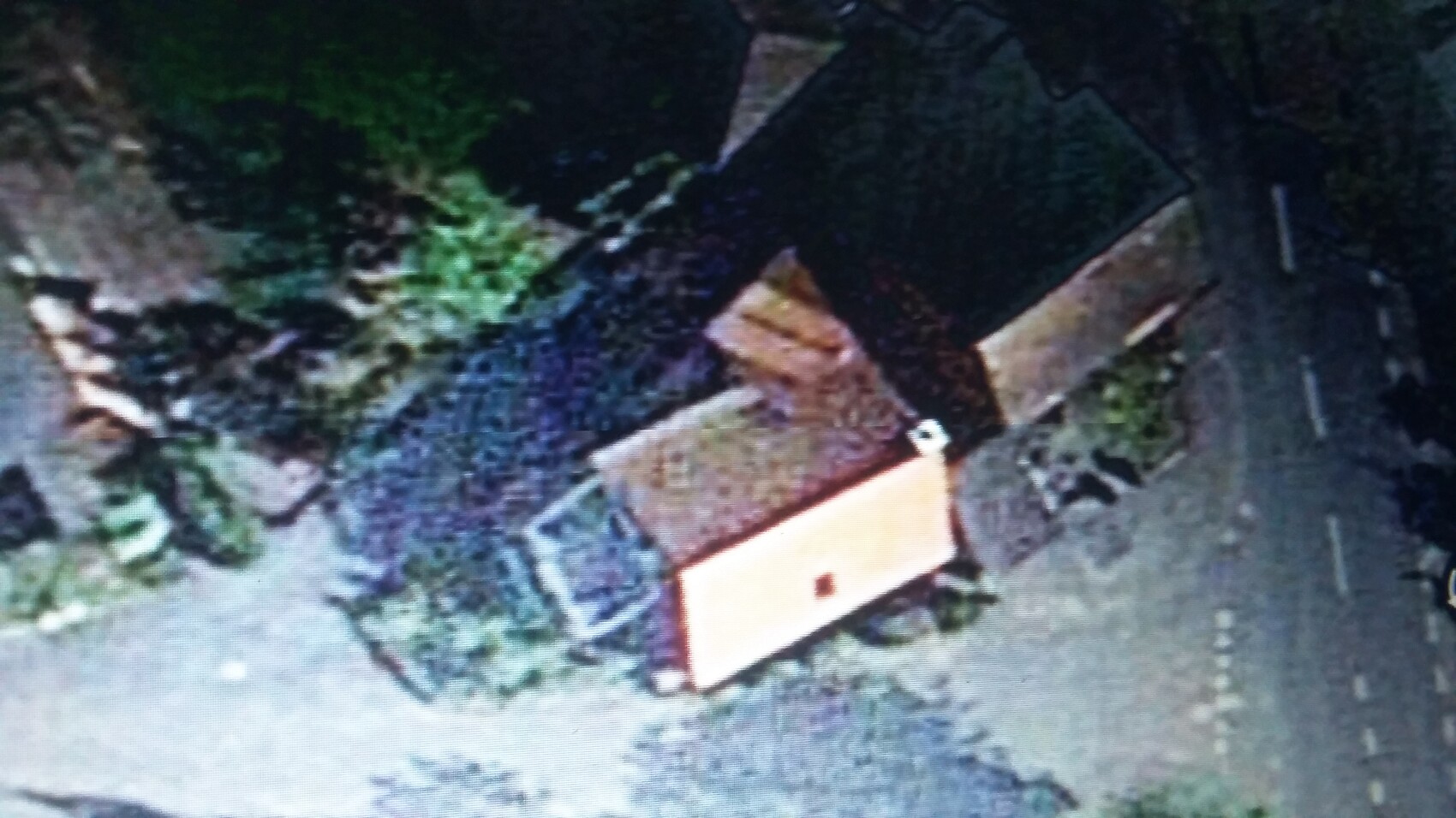 Vogelperspektive eines kleinen orangefarbenen Hauses mit dunklem Satteldach neben einer Straße