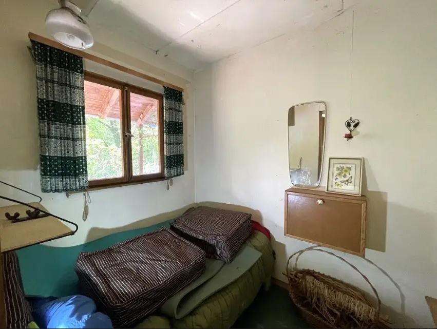 Kleines Schlafzimmer mit Fenster, Bett mit gestreiften Kissen, Spiegel und Bilderrahmen an der Wand.
