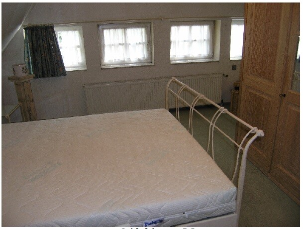 Kleines Schlafzimmer mit Metallbettgestell, Matratze und Holzschrank
