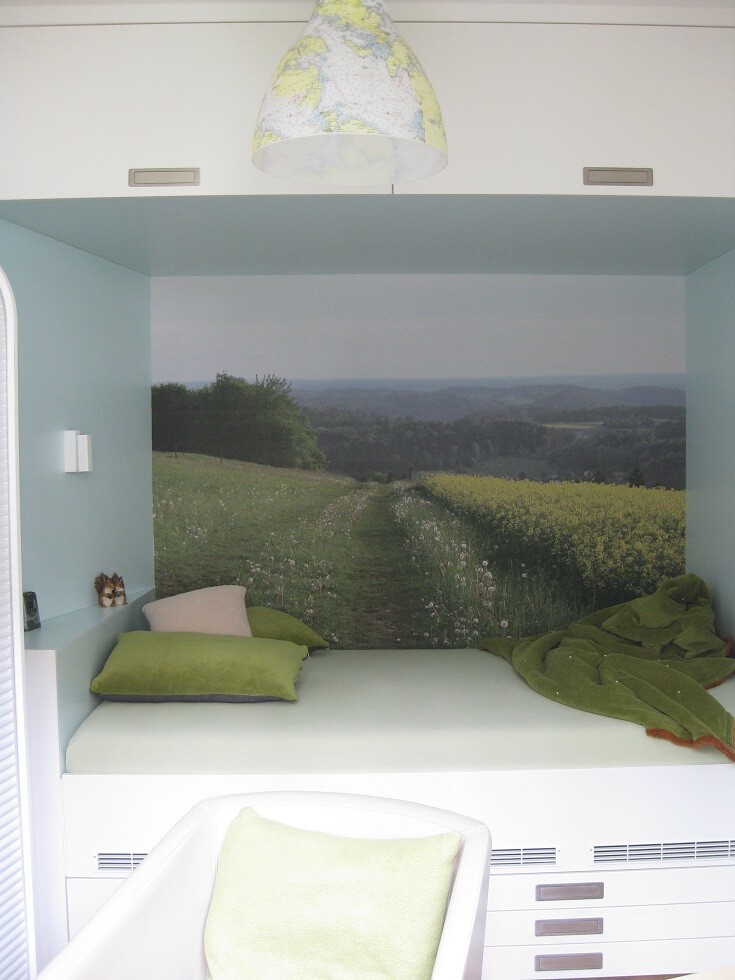 Bett in Nische mit Landschaftsmural: Wiesenweg, Hügel, grüne Kissen, Decke