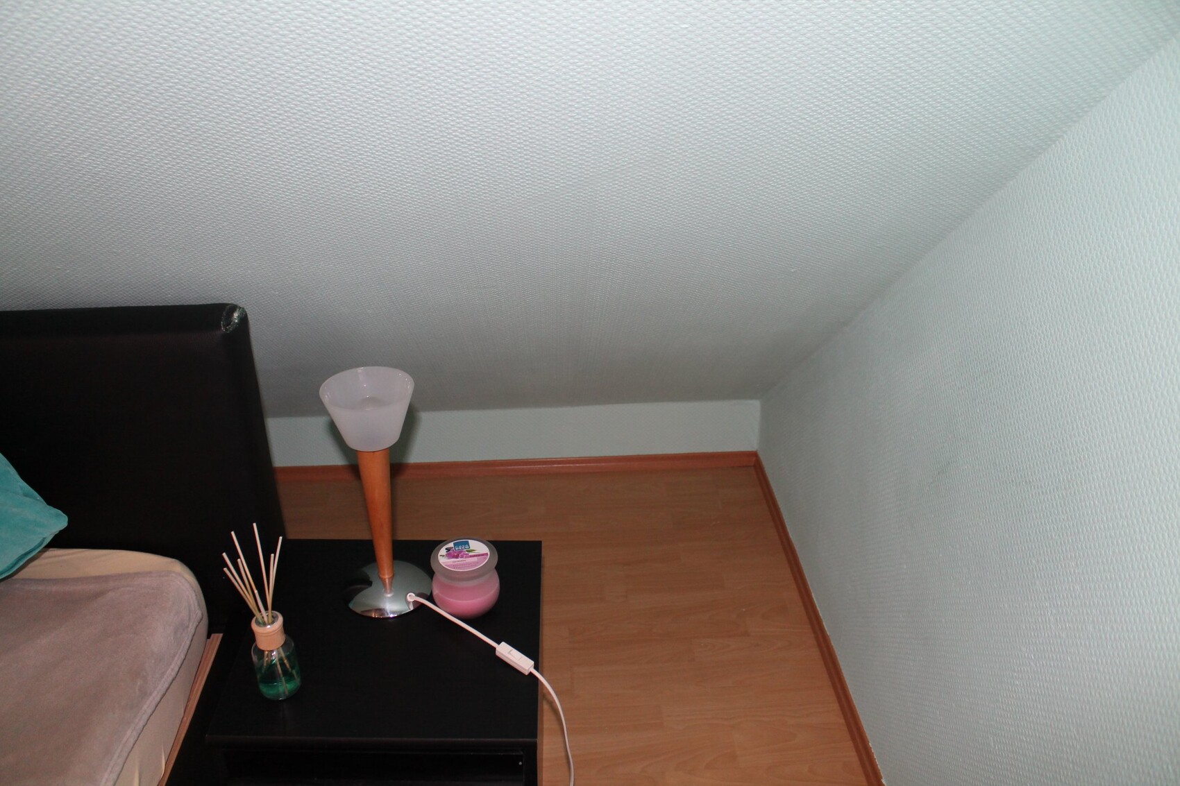 Kleines Schlafzimmer mit Nachttischlampe, Vase und Holzboden