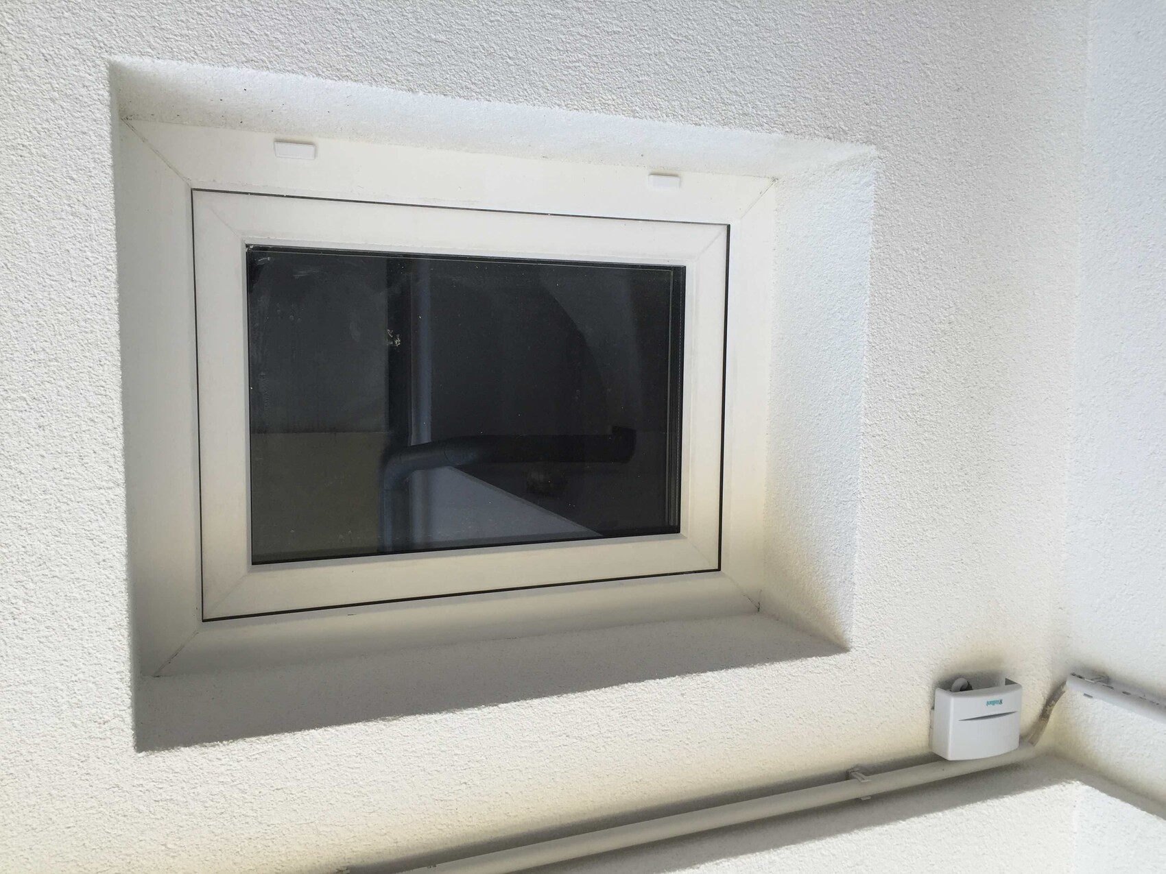 Kleines quadratisches Fenster in weisser Aussenwand, heller Rahmen, dunkles Glas