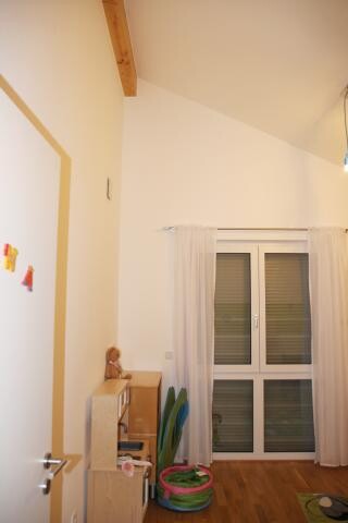 Kleines Wohnzimmer mit Holzboden, weißen Wänden, Fenster mit Vorhängen und Spielzeug.