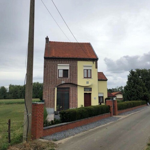 Zweistöckiges Haus mit Backstein- und Gelbfassade, rotem Ziegeldach, Vorgarten hinter Backsteinmauer.