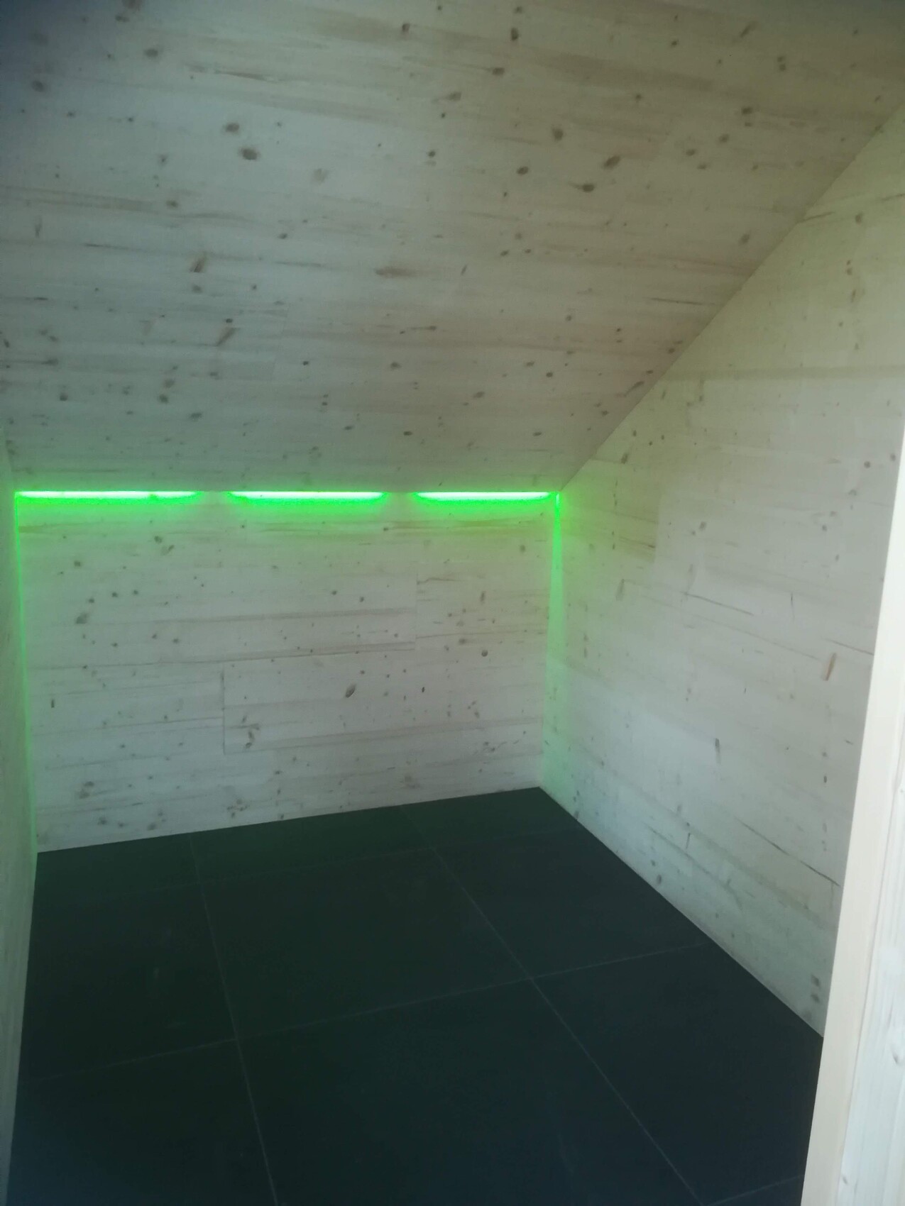 Kleines Zimmer mit hellen Holzwänden und grüner LED-Lichtleiste entlang der oberen Wandkante