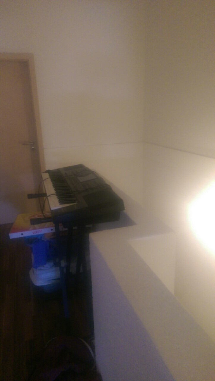 Kleines Zimmer mit elektronischem Keyboard auf Stativ, seitliche Wandbeleuchtung.