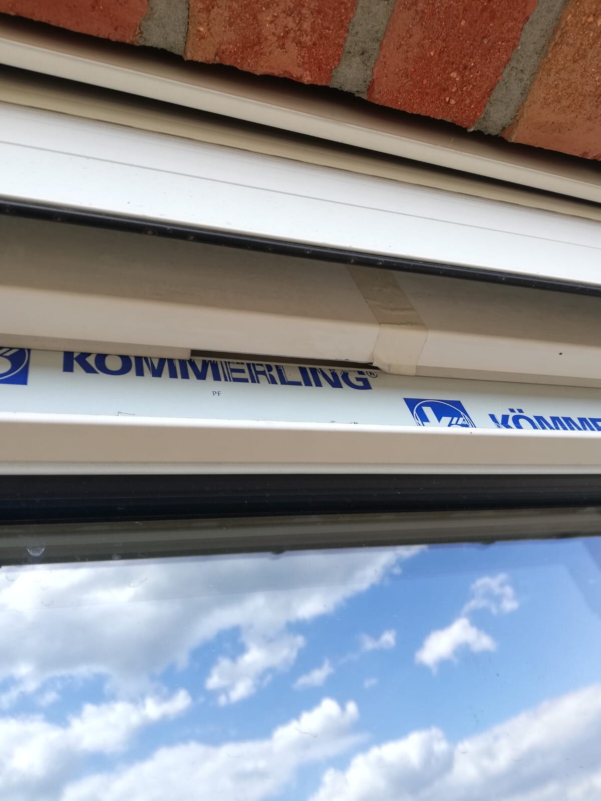 Weißer Kunststofffensterrahmen mit KOMMERLING-Logo; darüber eine Ziegelmauer.